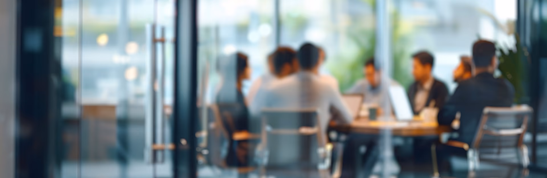 Blurred view of people sitting around a table in a modern office with hanging lights.