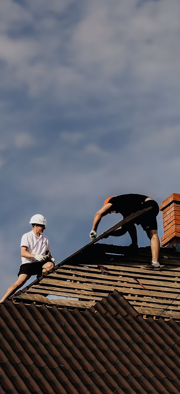 Two workers on a rooftop repairing a wooden framework under construction with tools.